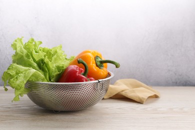 Photo of Colander with fresh lettuce and bell peppers on wooden table, space for text