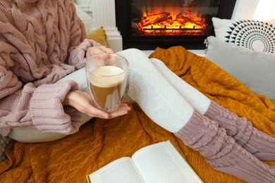 Photo of Woman with cup of coffee sitting near burning fireplace, closeup