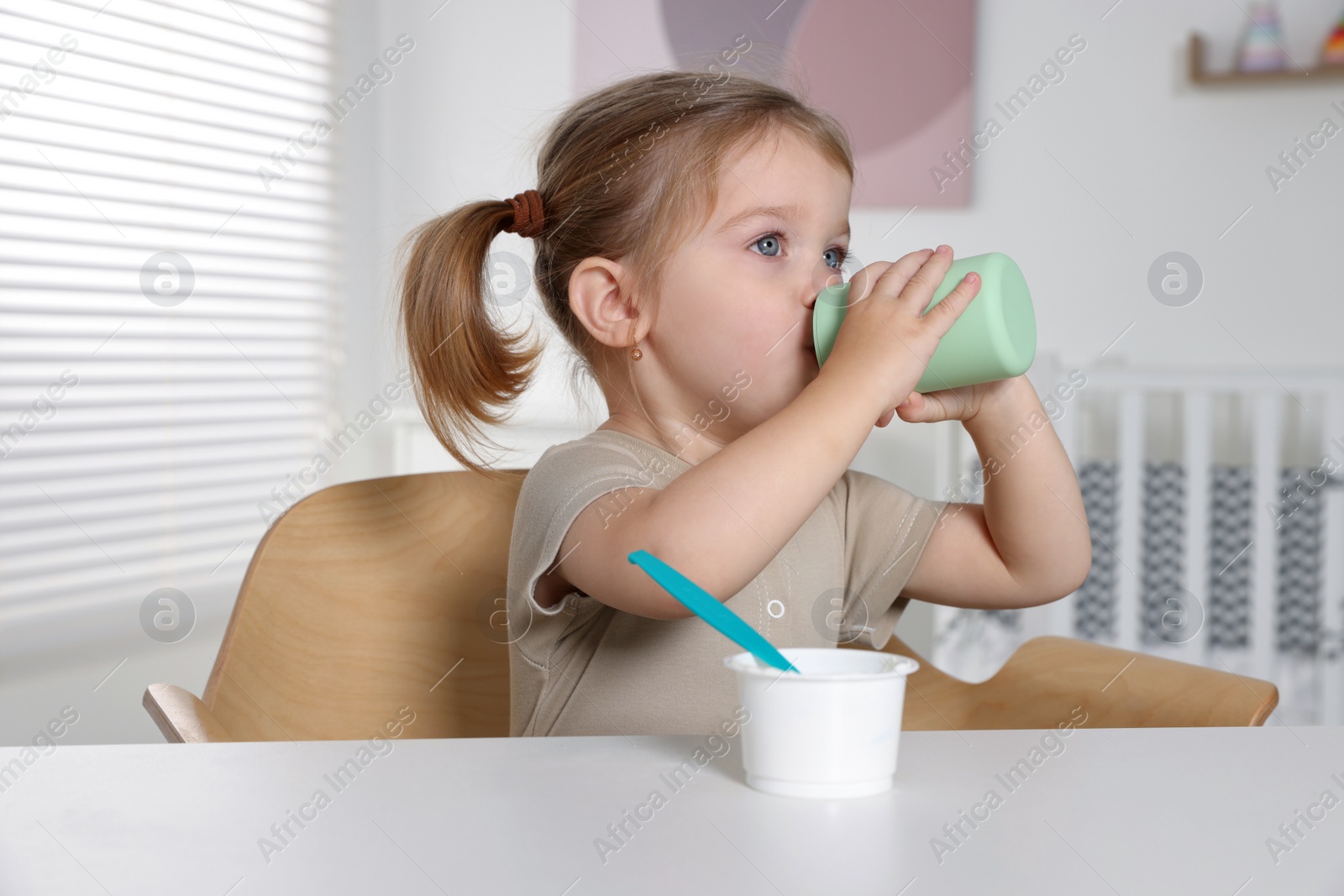 Photo of Cute little child with bottle and cup of tasty yogurt at white table indoors