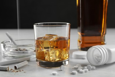 Photo of Alcohol and drug addiction. Whiskey in glass, cigarettes and pills on white table