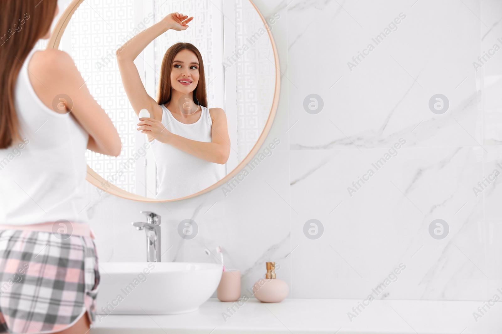 Photo of Beautiful young woman applying deodorant in bathroom. Space for text