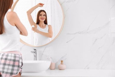 Beautiful young woman applying deodorant in bathroom. Space for text