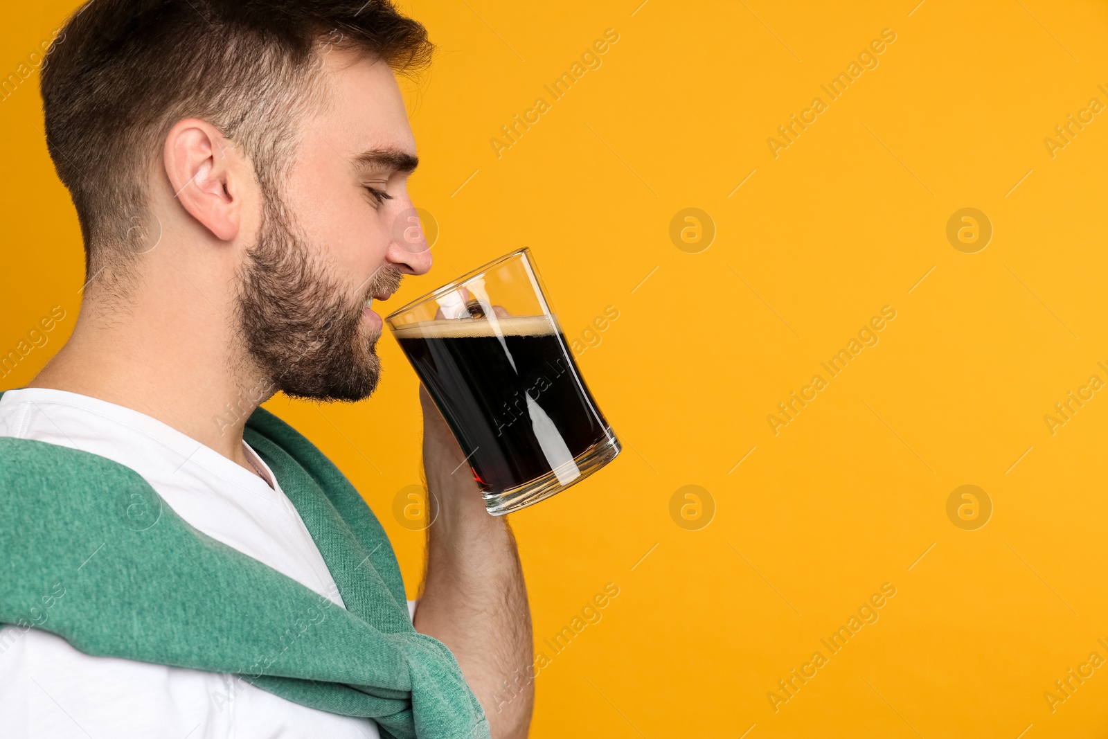 Photo of Handsome man with cold kvass on yellow background, space for text. Traditional Russian summer drink