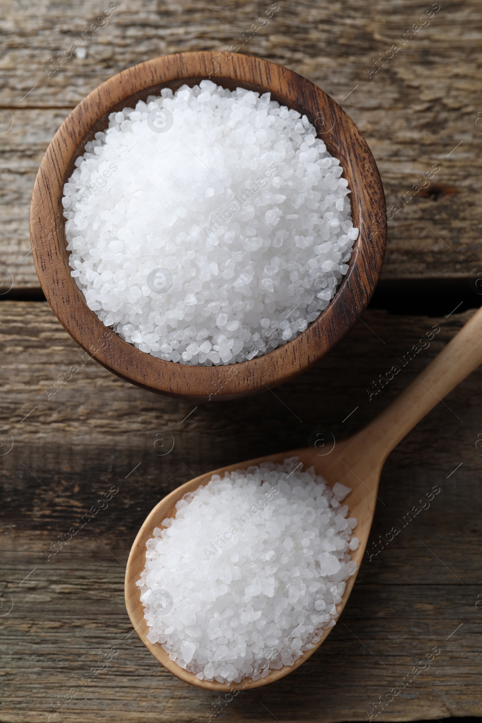 Photo of Organic salt in bowl and spoon on wooden table, flat lay