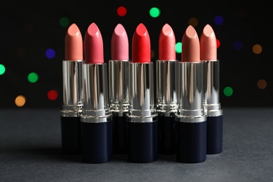 Photo of Different lipsticks on table against blurred lights. Cosmetic product