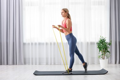 Photo of Athletic woman doing exercise with fitness elastic band on mat at home