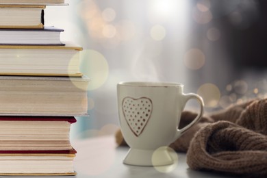 Stack of books and cup on table indoors. Bokeh effect 