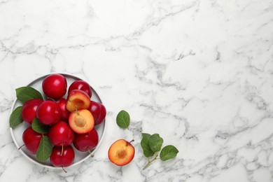 Delicious ripe cherry plums with leaves on white marble table, flat lay. Space for text