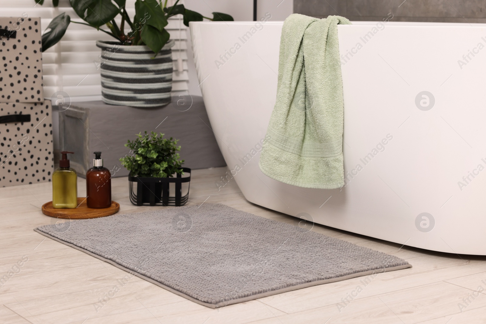 Photo of Soft bath mat, green plant and cosmetic products near tub in bathroom