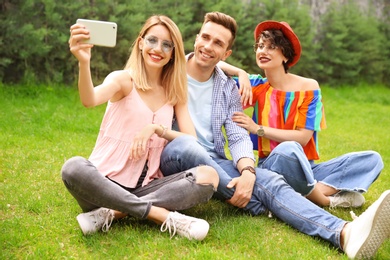 Group of friends in stylish clothes taking selfie outdoors