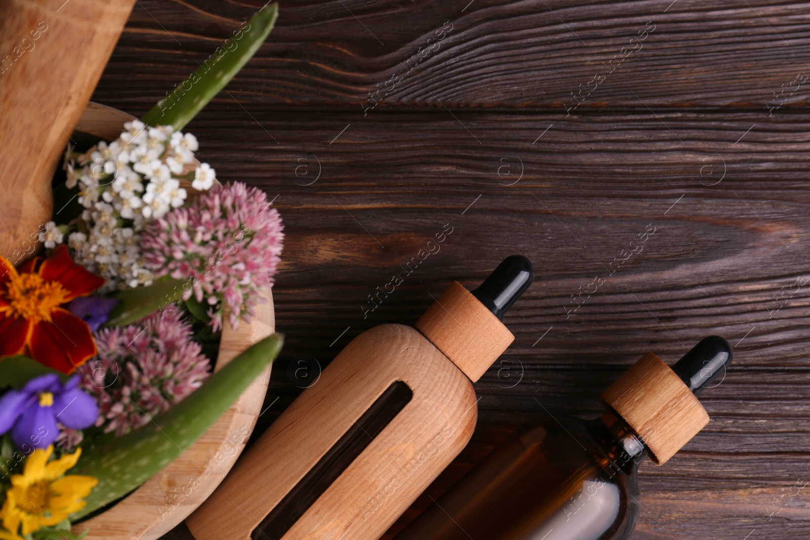 Photo of Glass bottles of aromatic essential oil and mortar with different herbs on wooden table, flat lay. Space for text