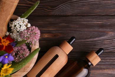 Glass bottles of aromatic essential oil and mortar with different herbs on wooden table, flat lay. Space for text