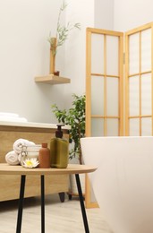 Photo of Different spa products on table near ceramic tub in bathroom