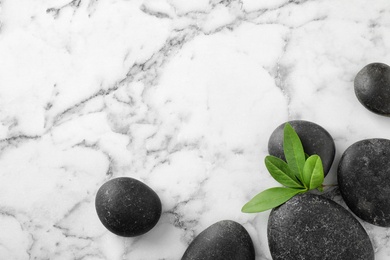 Photo of Black spa stones with green branch on marble background, flat lay. Space for text