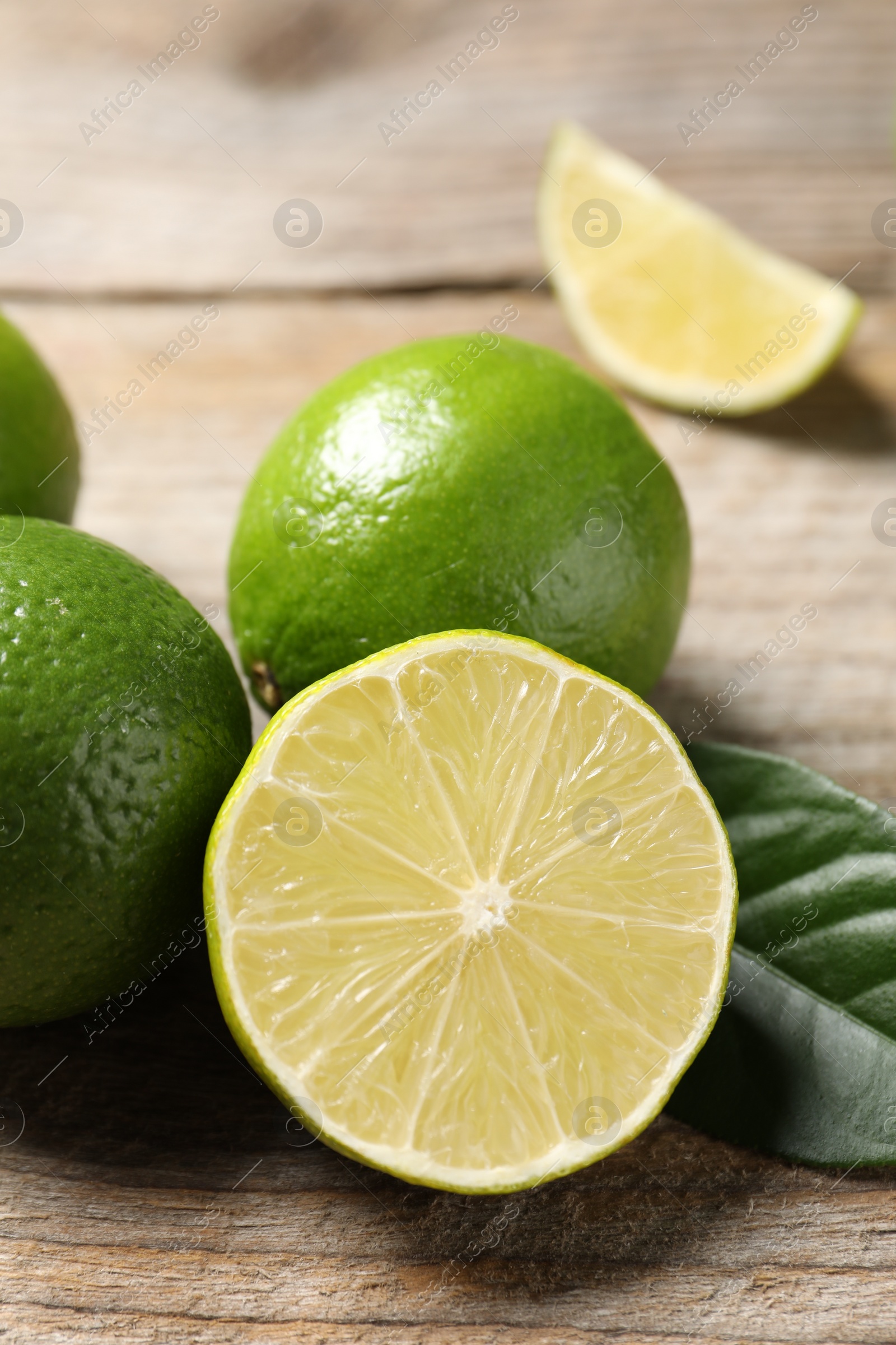 Photo of Whole and cut fresh limes on wooden table, closeup