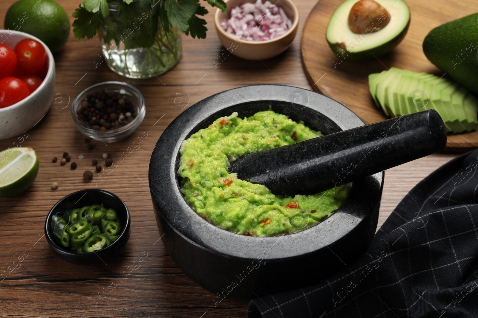 Photo of Delicious guacamole in mortar and ingredients on wooden table, closeup