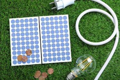 Photo of Flat lay composition with solar panels, light bulb and coins on green grass