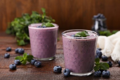 Photo of Glasses of blueberry smoothie with fresh berries and mint on wooden table, space for text