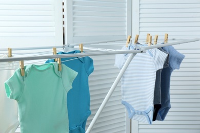 Photo of Different cute baby onesies hanging on clothes line indoors. Laundry day