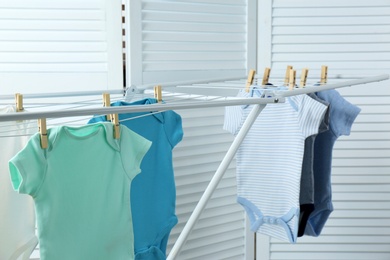 Different cute baby onesies hanging on clothes line indoors. Laundry day