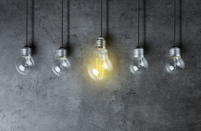 Image of Idea concept. Glowing light bulb among others on grey background