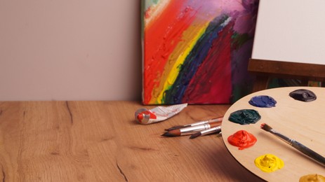 Photo of Artist's palette with samples of colorful paints and brush on wooden table. Space for text