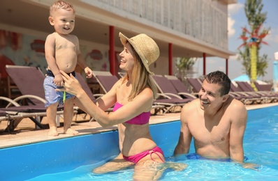 Happy family with little child resting in swimming pool outdoors