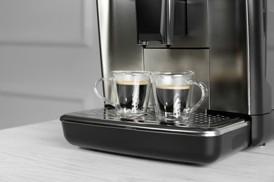 Photo of Modern espresso machine with cups of coffee on white wooden table, closeup