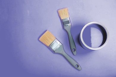 Tin can with paint and brushes on violet background, flat lay. Space for text