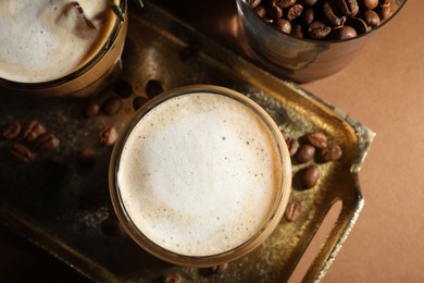 Refreshing iced coffee with milk in glasses and beans on brown table, flat lay