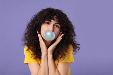Photo of Beautiful young woman blowing bubble gum on purple background