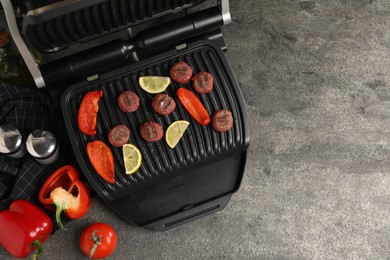 Photo of Electric grill with meat balls, bell peppers and lemon on grey textured table, flat lay. Space for text