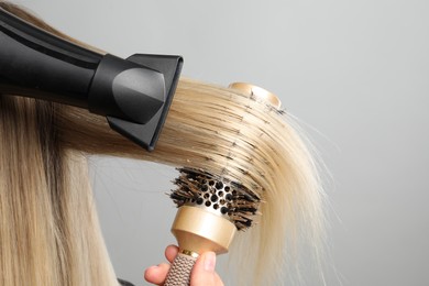 Photo of Hairdresser blow drying client's hair on light grey background, closeup