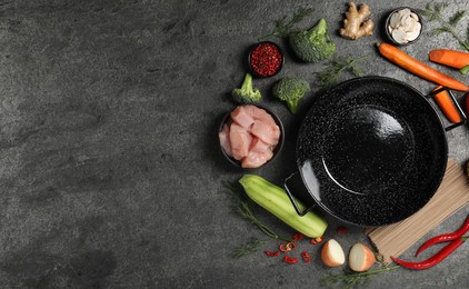 Photo of Empty iron wok surrounded by ingredients on grey table, flat lay. Space for text