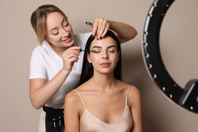 Photo of Professional makeup artist working with beautiful young woman on beige background. Using ring lamp