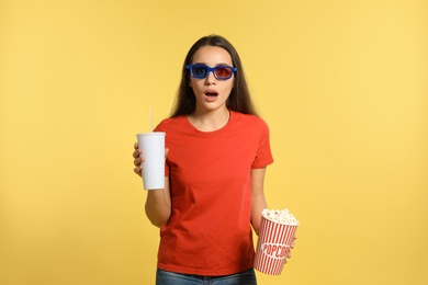 Photo of Emotional woman with 3D glasses, popcorn and beverage during cinema show on color background