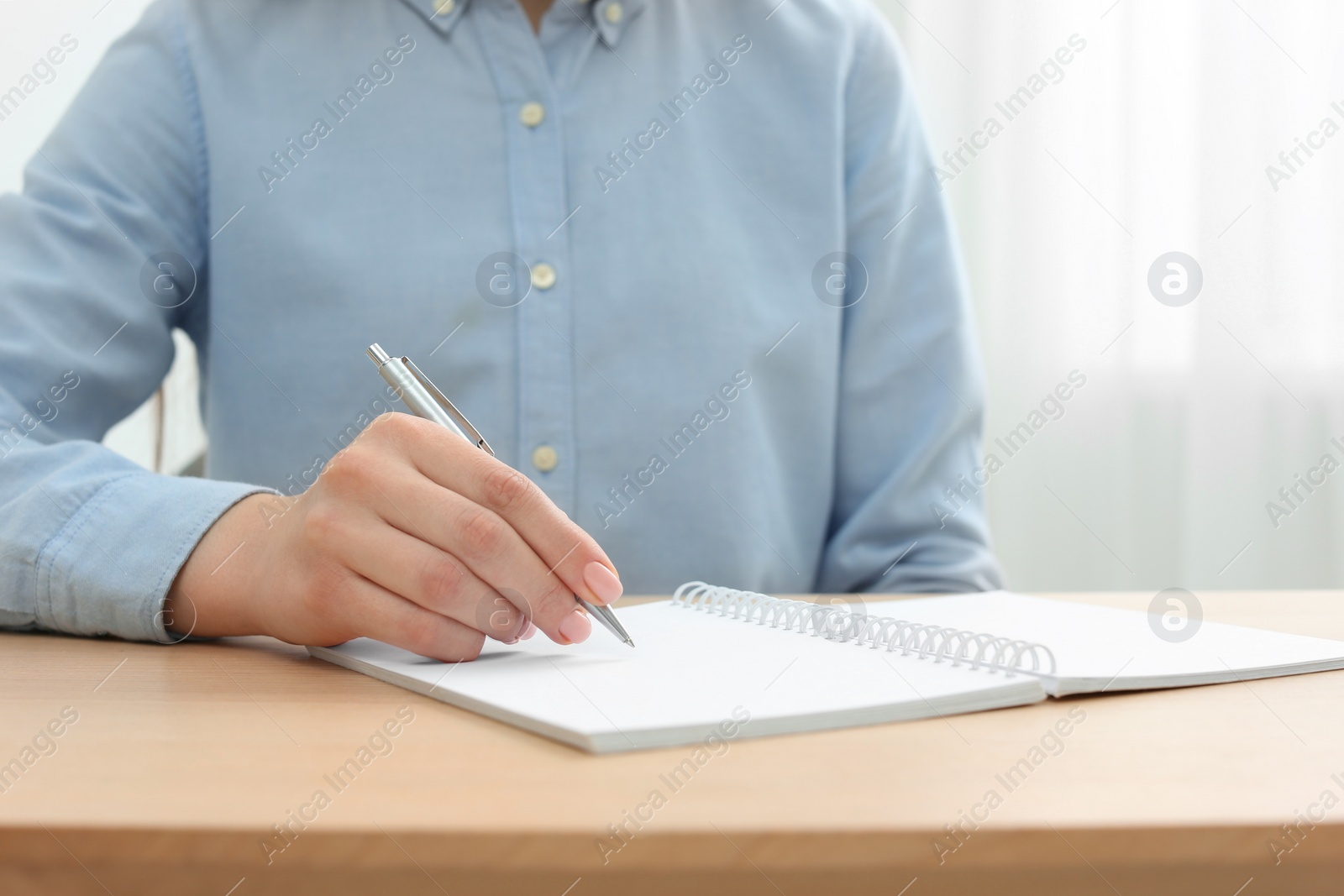 Photo of Woman writing in notebook at wooden table, closeup