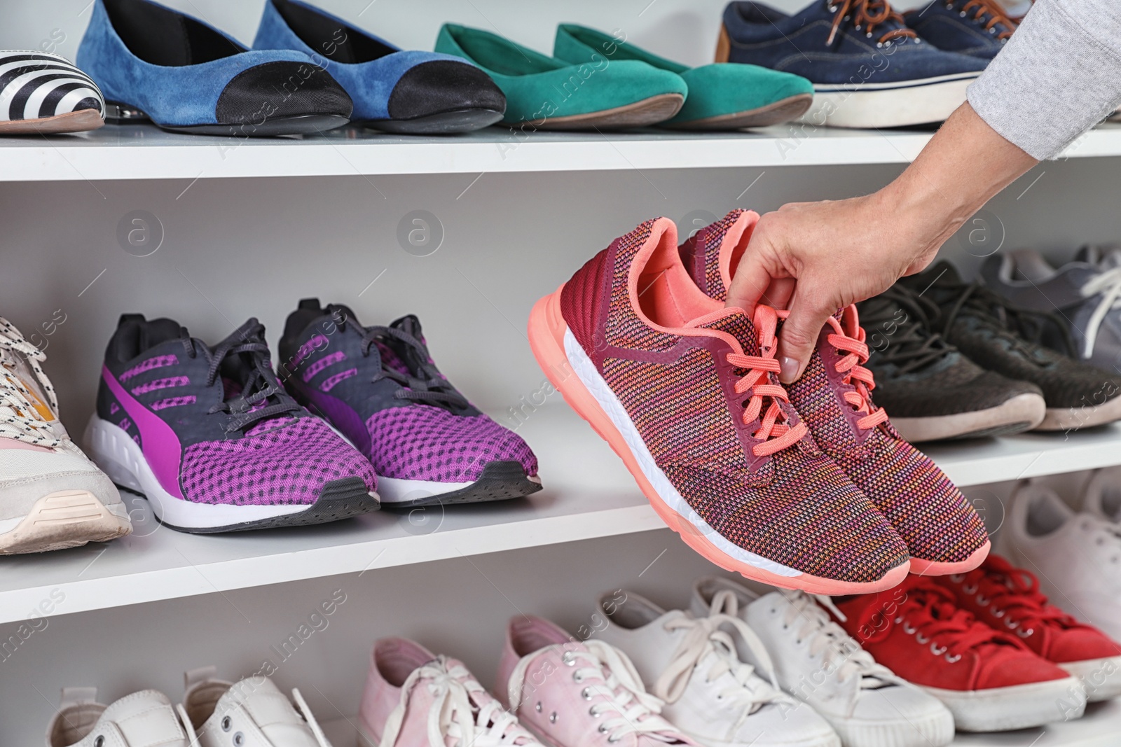 Photo of Woman taking sneakers from shelving unit, closeup