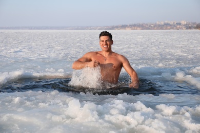 Photo of Man immersing in icy water on winter day. Baptism ritual