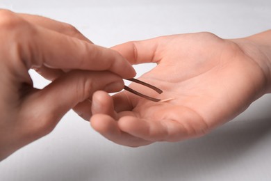 Photo of Woman pulling splinter from hand using tweezers on white background, closeup