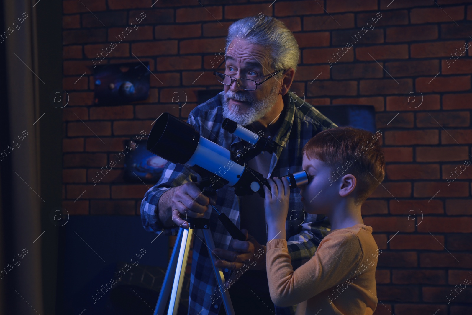 Photo of Little boy with his grandfather looking at stars through telescope in room