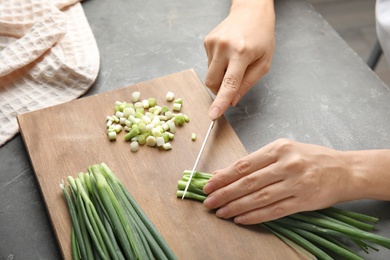 Photo of Woman cutting fresh green onion on wooden board