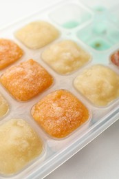 Photo of Different fruit puree in ice cube tray on white table, closeup