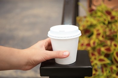 Woman with cardboard cup of coffee near flower bed outdoors, closeup