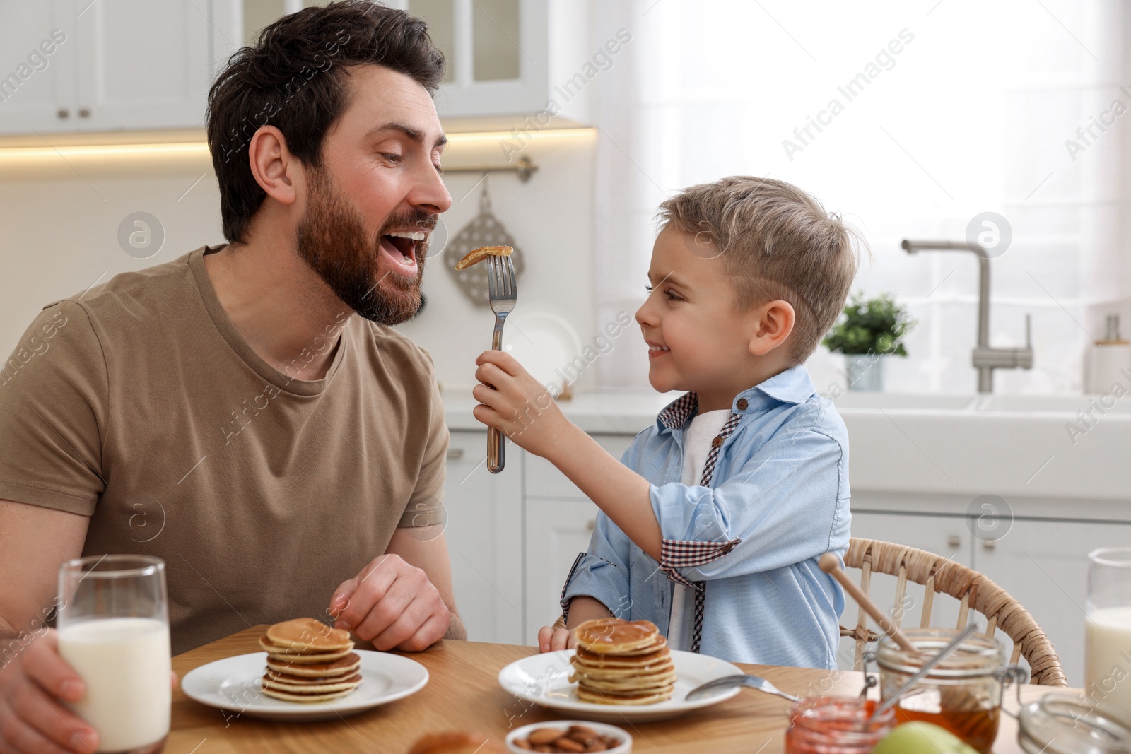 Photo of Father and his cute little son having breakfast at table in kitchen