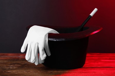 Photo of Black top hat, gloves and wand on wooden table. Magician equipment