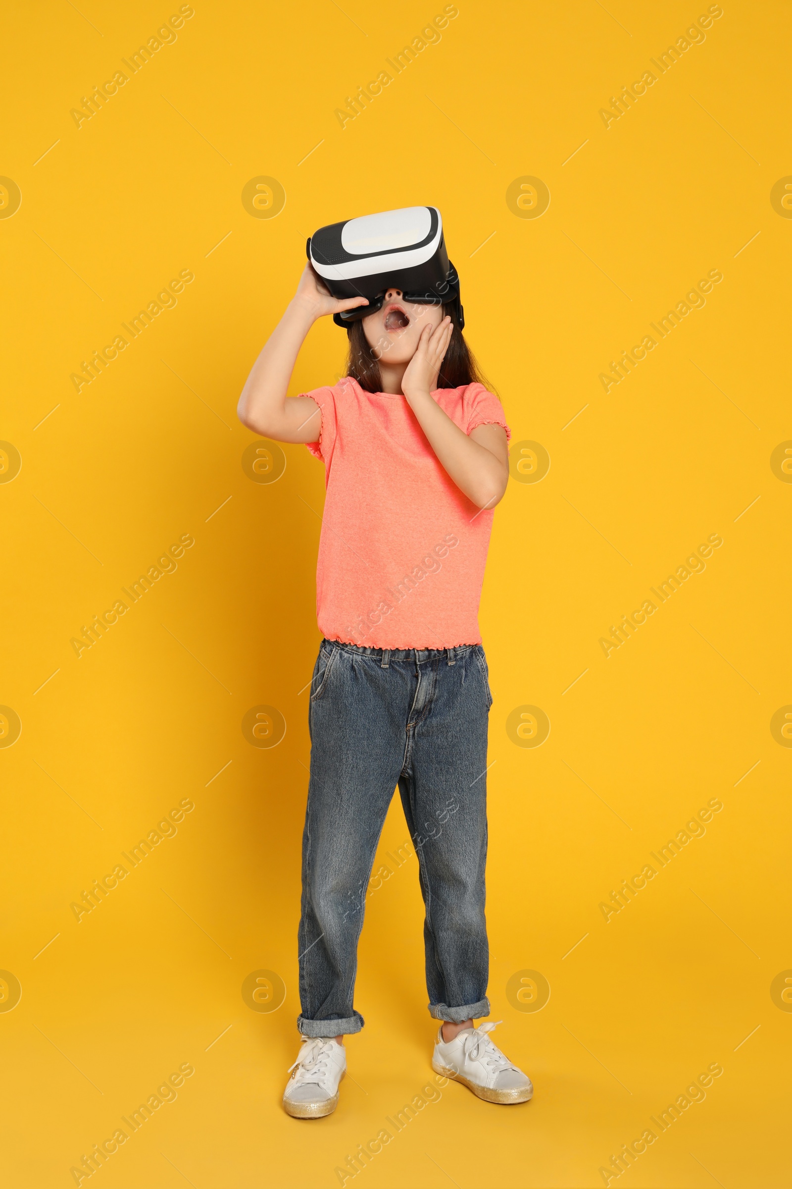 Photo of Emotional little girl using virtual reality headset on yellow background