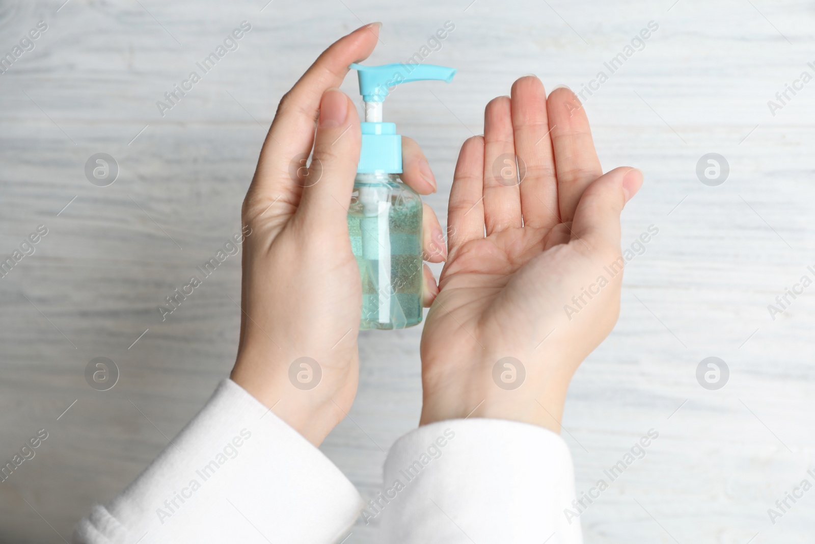 Photo of Woman applying antiseptic gel on hand against light background, above view