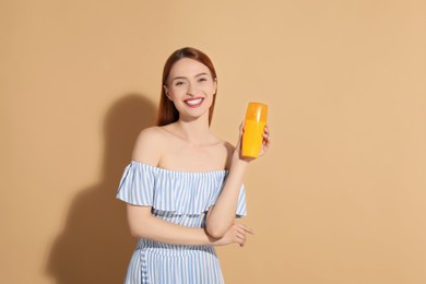 Photo of Beautiful young woman holding sun protection cream on beige background, space for text