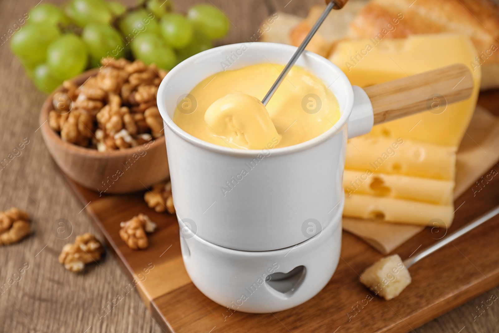 Photo of Pot of tasty cheese fondue and fork with bread on wooden table